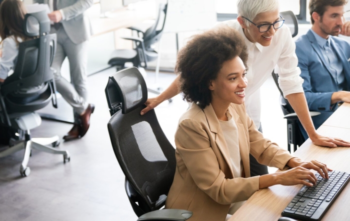 Two business colleagues collaborate at a workstation in a modern office, reviewing AI tool usage across the organization to identify shadow AI exposure.